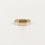 A minimalist gold signet ring with a flat, polished rectangular face, shown on a clean white background.