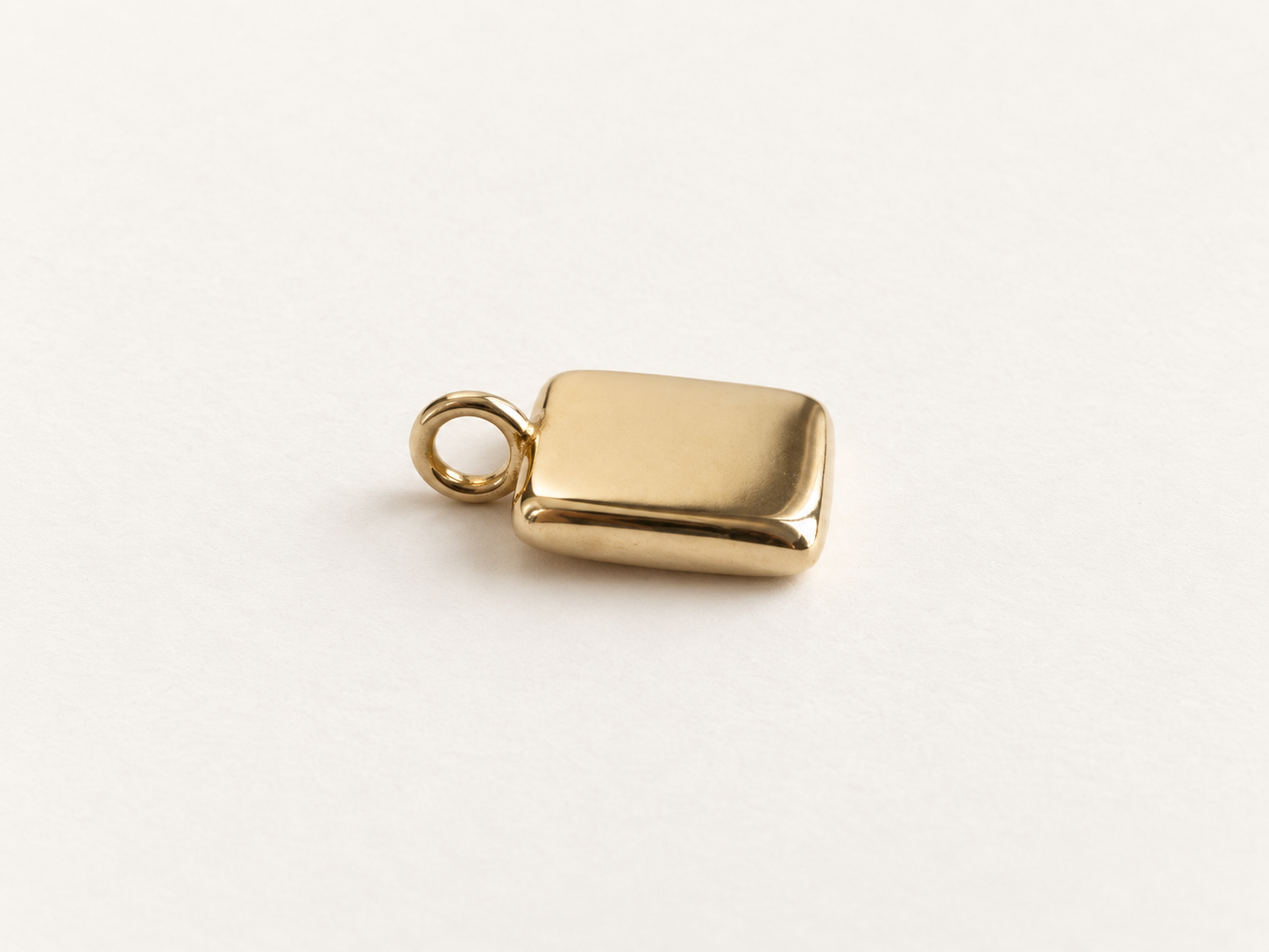 A small polished gold rectangular pendant charm with rounded corners and a loop at the top, photographed on a clean white background.