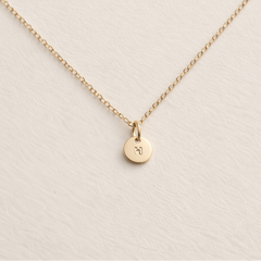 Gold necklace with a small round pendant on a beige background