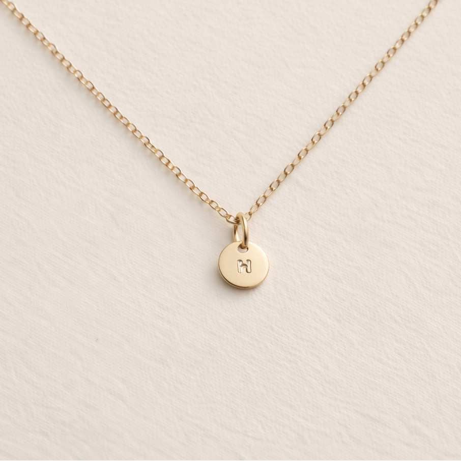 Gold necklace with a small round pendant on a beige background