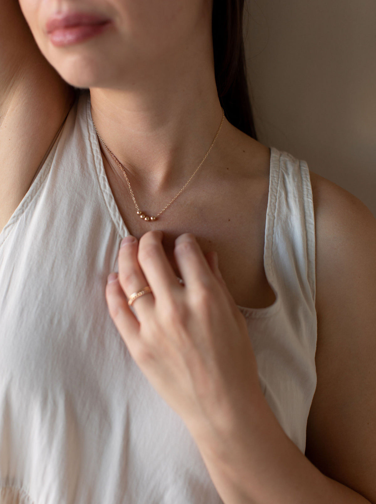 Model wearing a delicate gold bead necklace and gold ring with an ivory blouse.