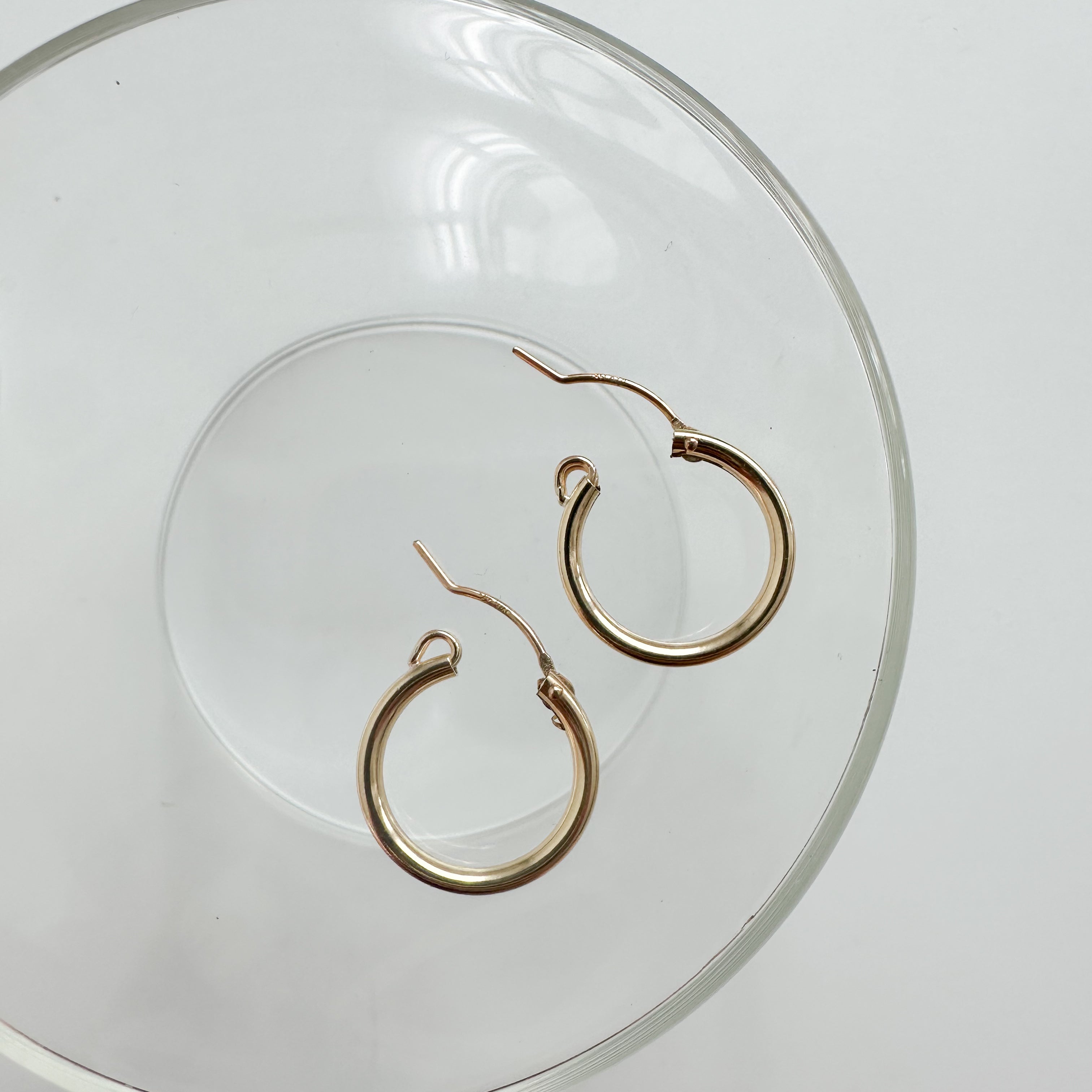 Gold-filled click hoop earrings arranged on a clear glass dish for a minimal aesthetic.