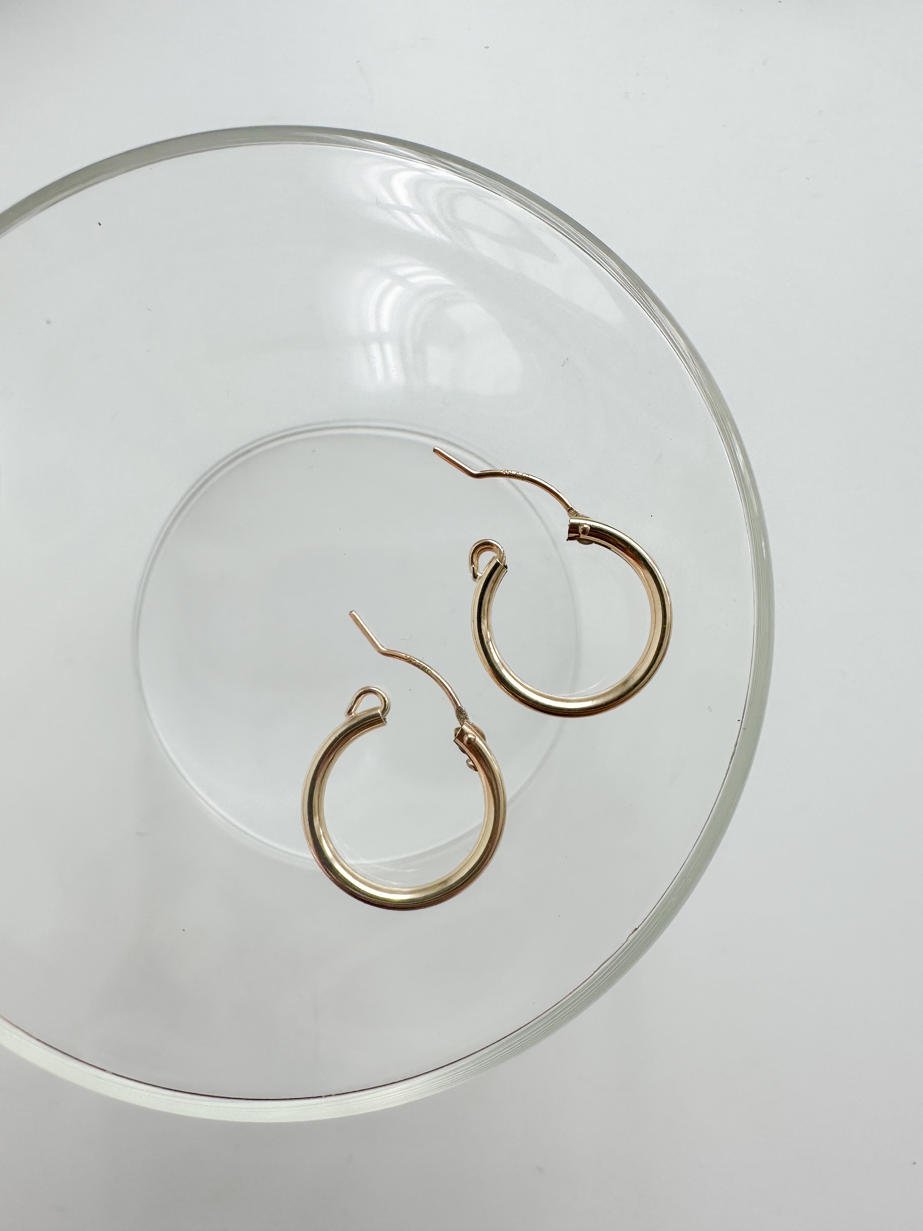 Gold-filled click hoop earrings arranged on a clear glass dish for a minimal aesthetic.