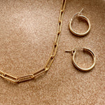 Gold-filled hoop earrings displayed on textured fabric with a gold necklace.