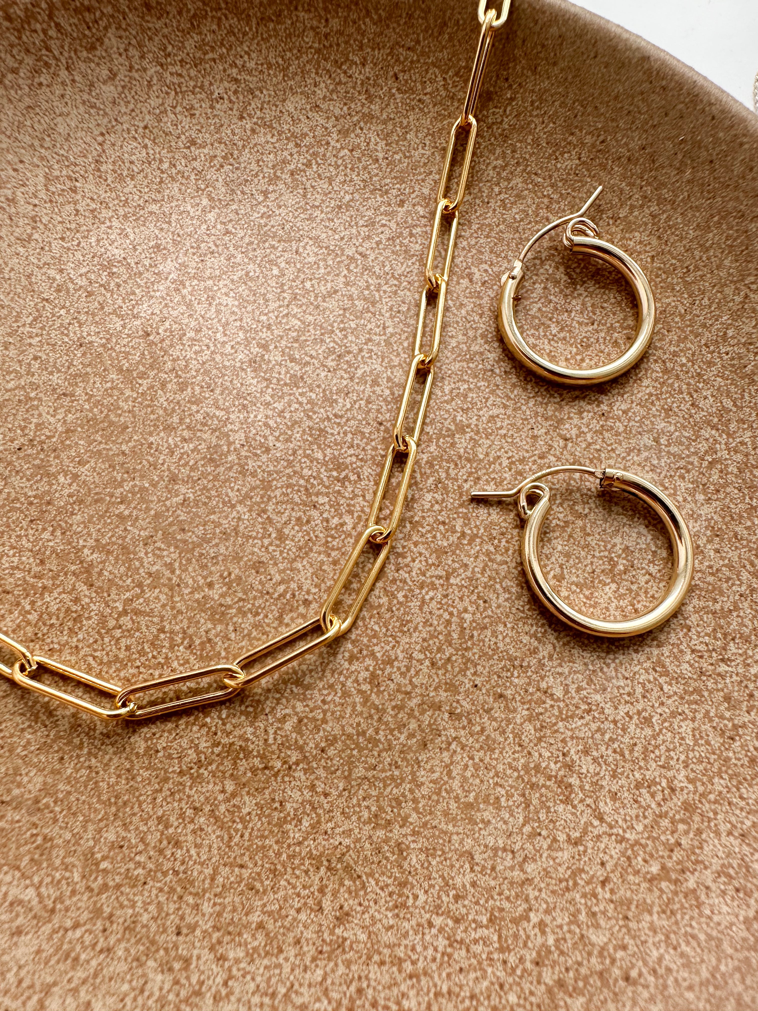 Gold-filled hoop earrings displayed on textured fabric with a gold necklace.