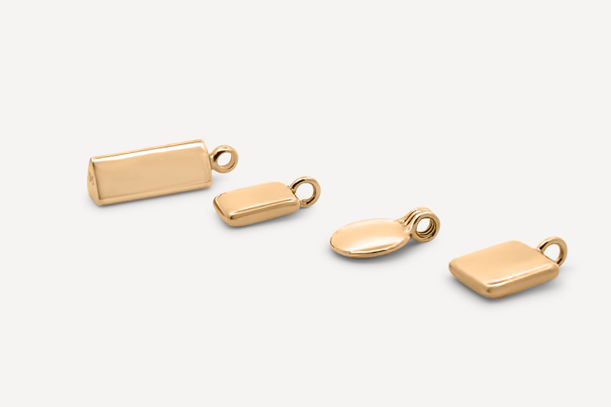 A collection of four solid gold pendant charms in varying shapes, including a rectangle, oval, and square design, arranged on a neutral background.