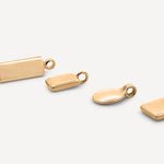 A collection of four solid gold pendant charms in varying shapes, including a rectangle, oval, and square design, arranged on a neutral background.