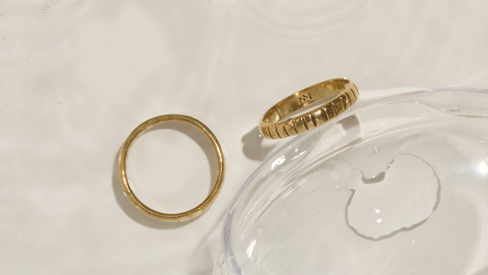 Solid gold rings displayed on translucent surface highlighting jewelry materials and care guide, featuring textured and smooth gold band designs with elegant typography overlay