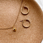 Lou Puff Heart Necklace in gold fill, layered with other jewelry to showcase its versatility and delicate charm.