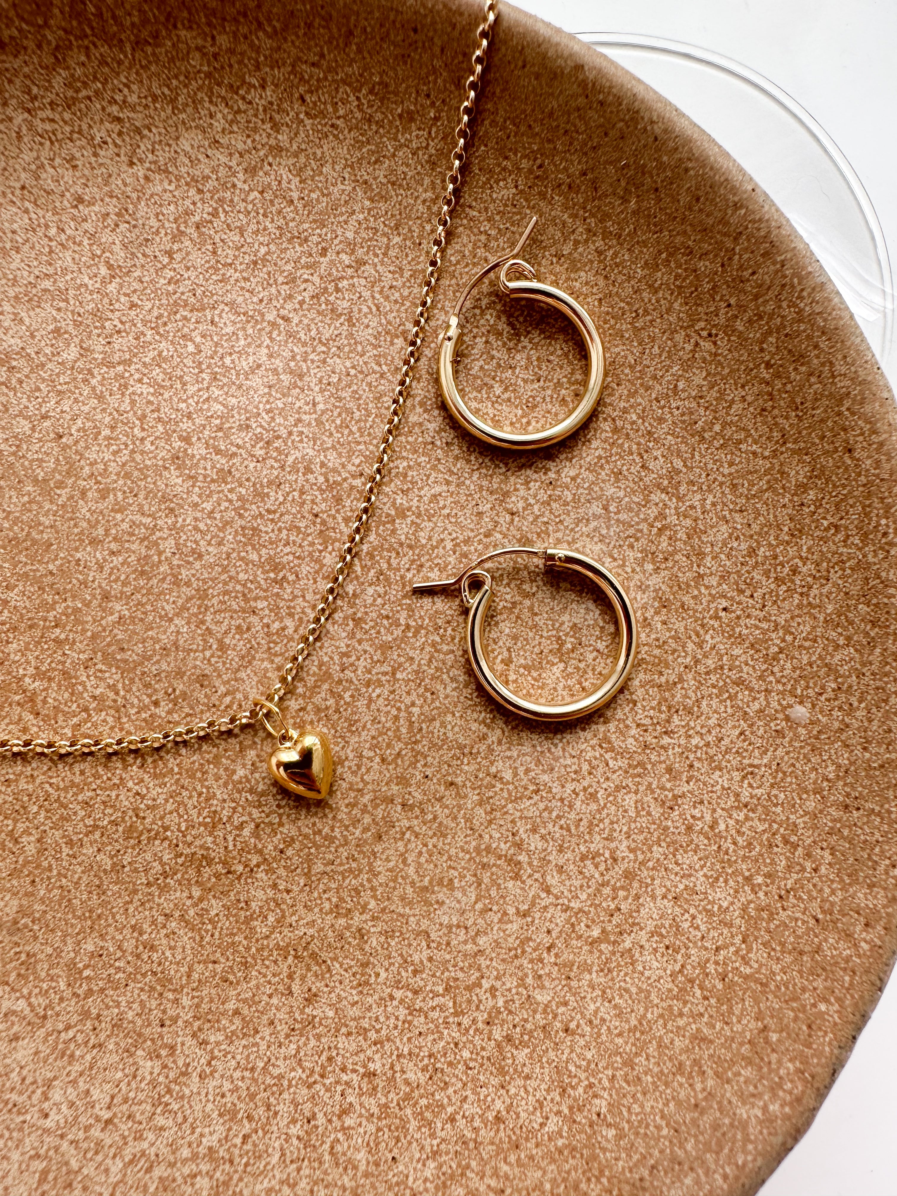 Lou Puff Heart Necklace in gold fill, layered with other jewelry to showcase its versatility and delicate charm.