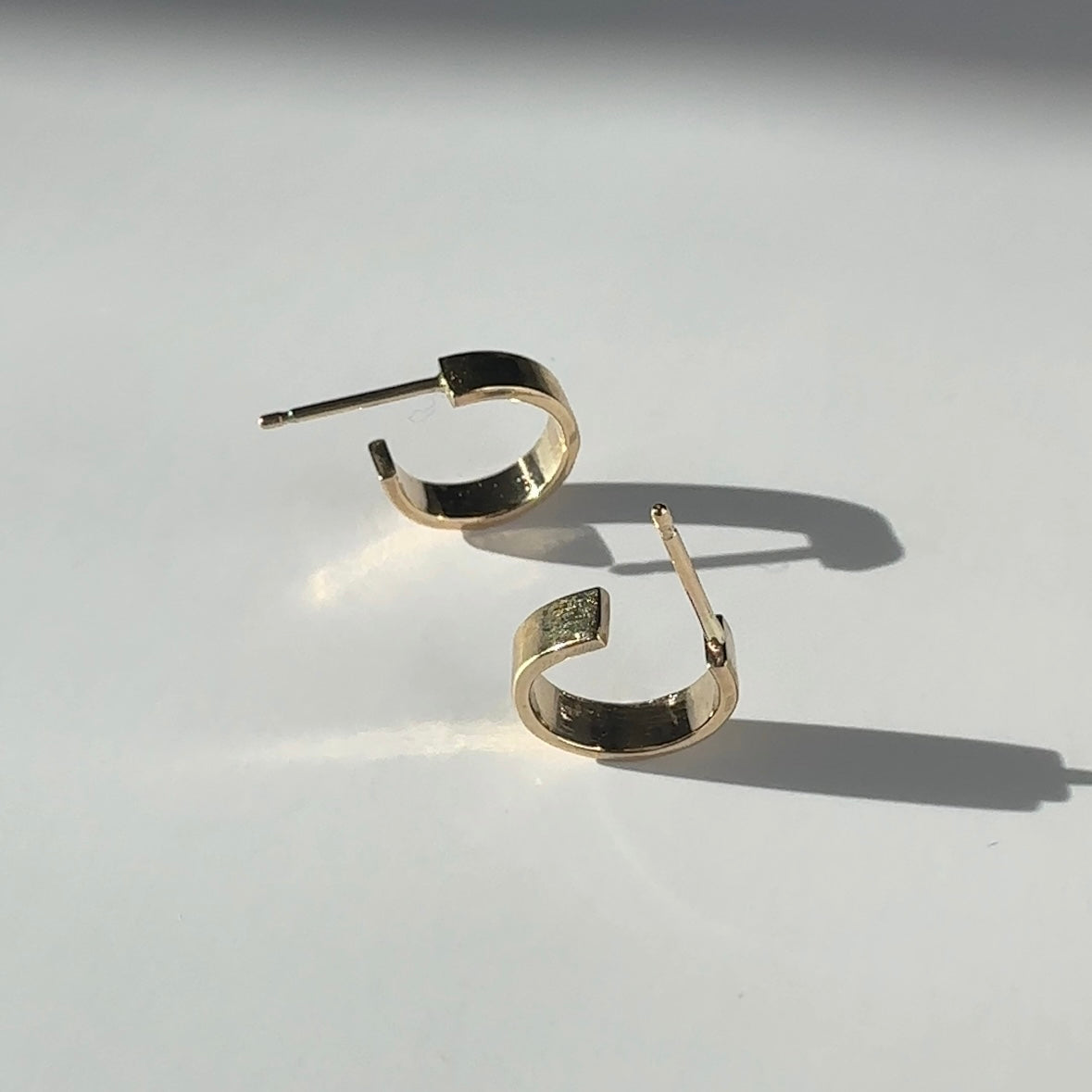 Petite Flat Hoops in solid 14k gold, showcasing a sleek and minimalist design on a clean surface.