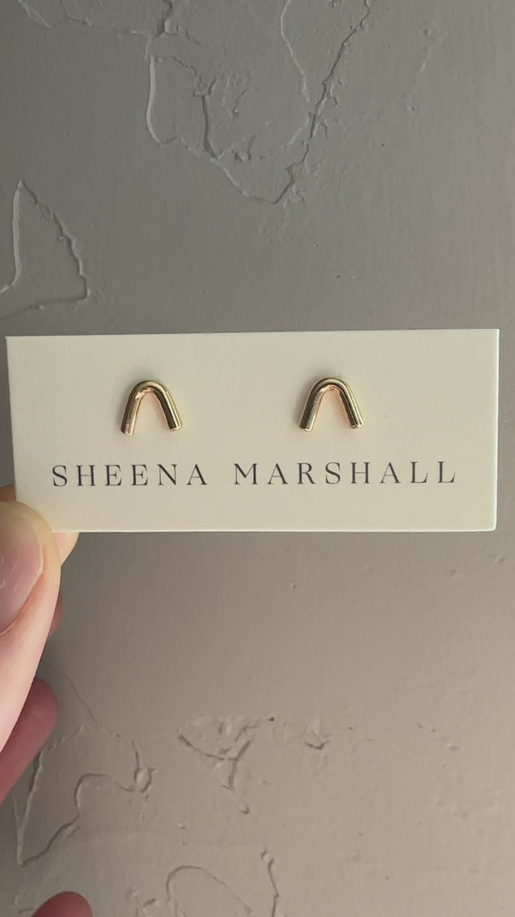 Handcrafted 14k gold arch stud earrings by Sheena Marshall Jewelry, measuring 7mm in height and 8.5mm in width, featuring an architectural design for refined casual elegance and heirloom quality shown on jewelry card.