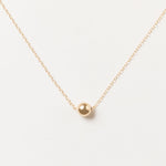 Nova Floating Sphere Necklace in gold fill with polished 11mm sphere displayed in a flat lay.
