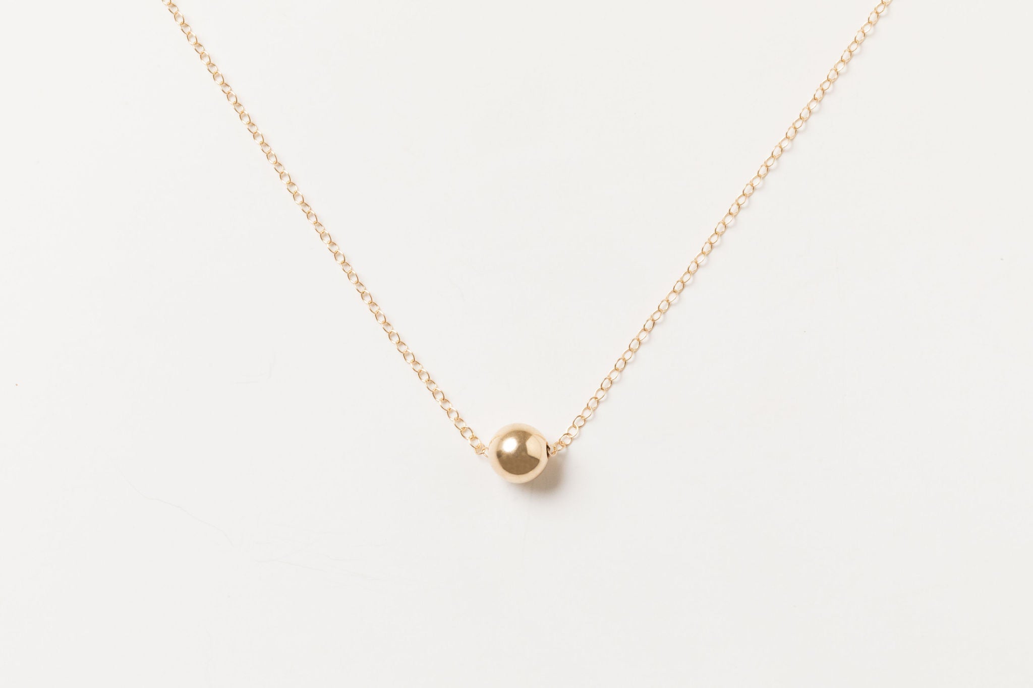 Nova Floating Sphere Necklace in gold fill with polished 11mm sphere displayed in a flat lay.