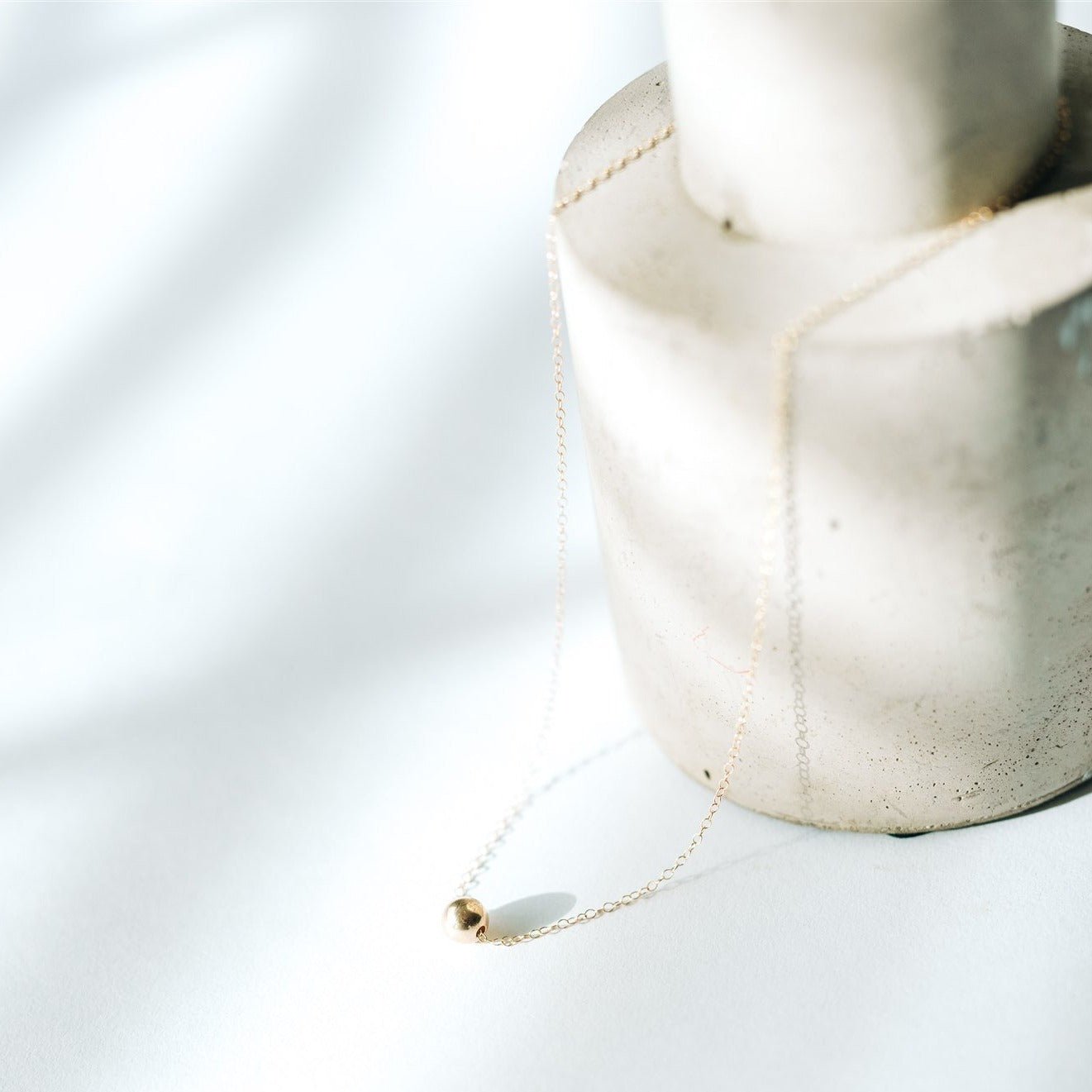 Nova Floating Sphere Necklace in gold fill with polished 11mm sphere displayed in a flat lay.