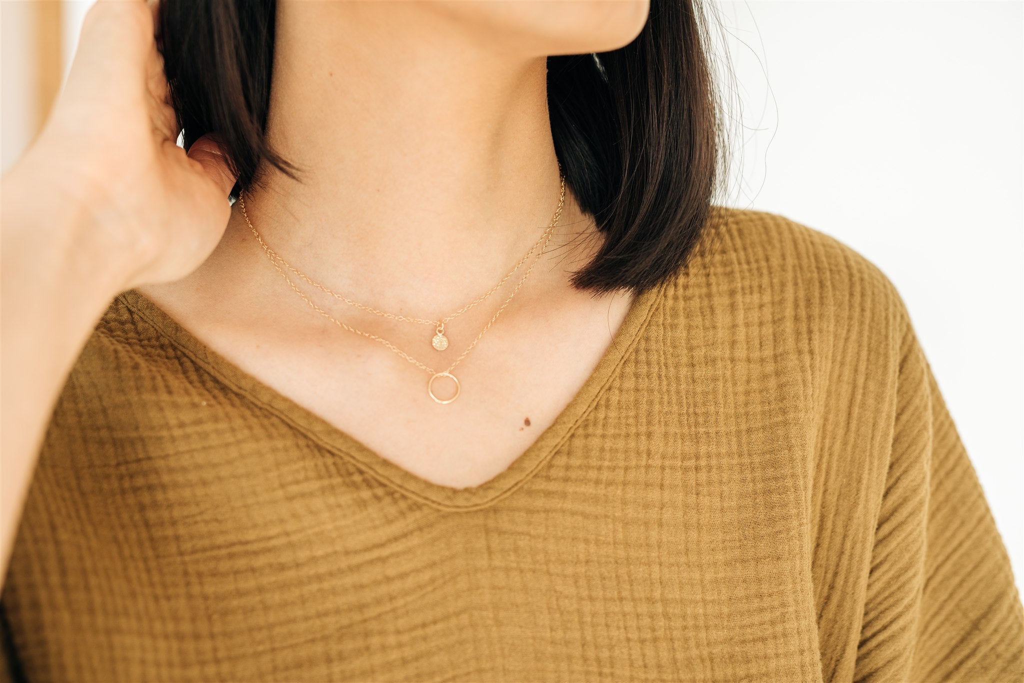 Woman wearing the Sol Circle Pendant Necklace layered with another necklace.