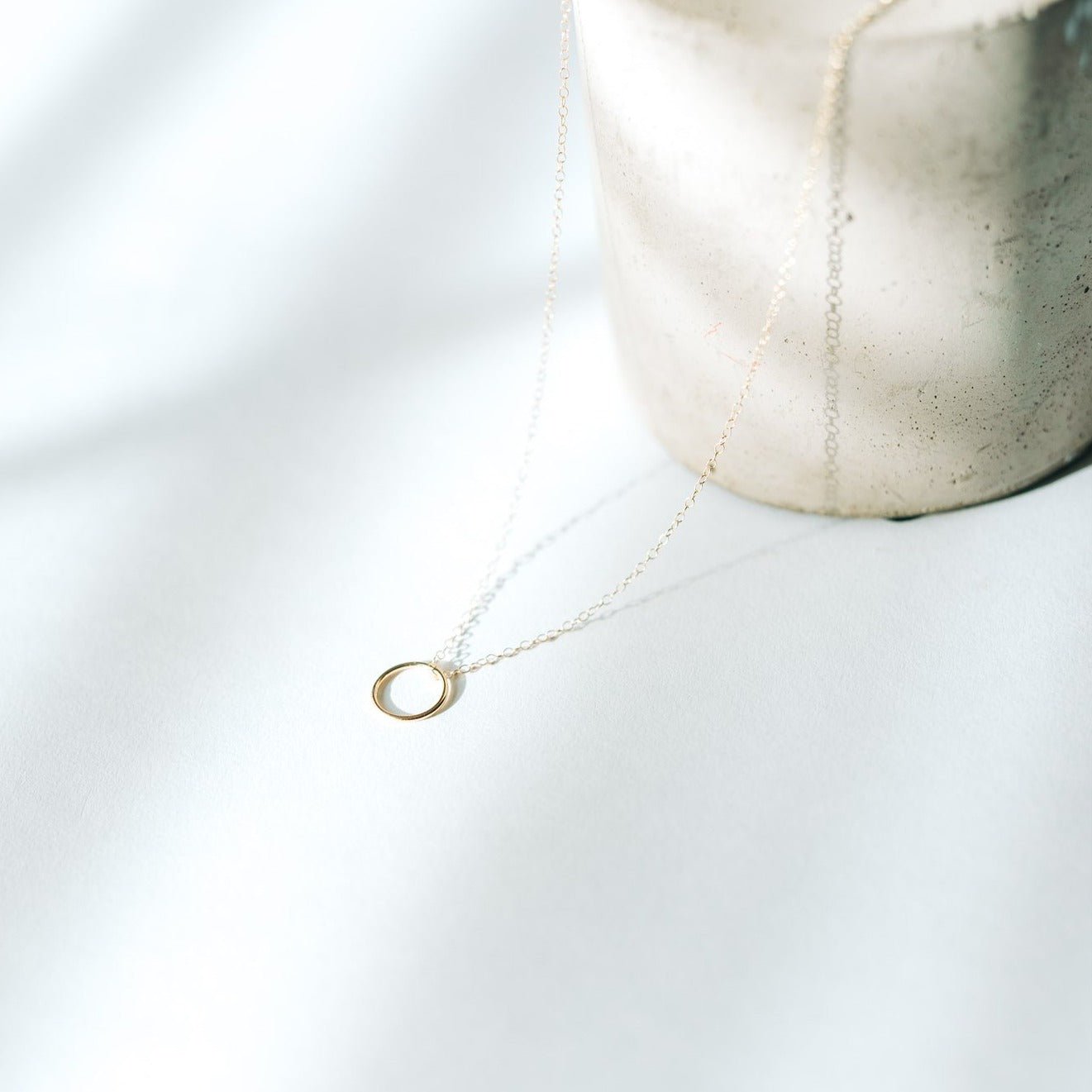 Sol Circle Pendant Necklace in gold fill photographed in natural light with a shadowed background.