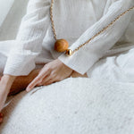 Cozy close-up of Sheena Marshall's Sandalwood Bead Necklace, handmade with a gold-filled chain and ethically sourced sandalwood bead for a refined look.
