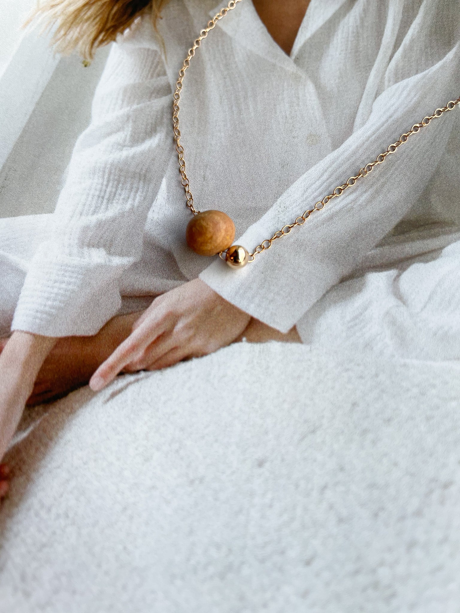 Cozy close-up of Sheena Marshall's Sandalwood Bead Necklace, handmade with a gold-filled chain and ethically sourced sandalwood bead for a refined look.
