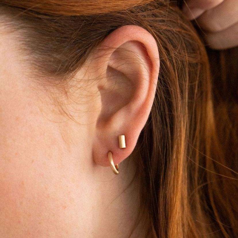 Tube stud earrings in solid gold worn on ear, showcasing their refined and understated design.